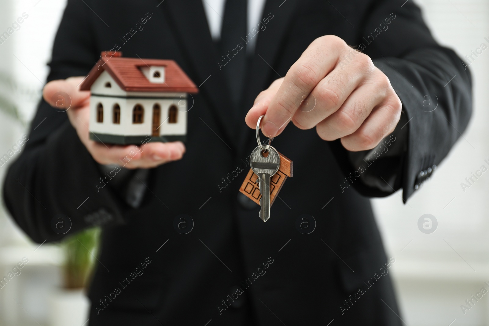 Photo of Real estate agent holding house model and key indoors, closeup