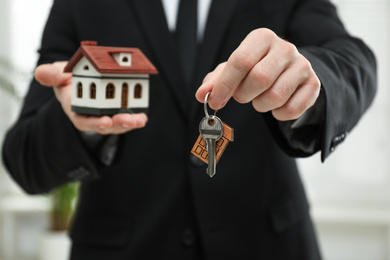 Real estate agent holding house model and key indoors, closeup