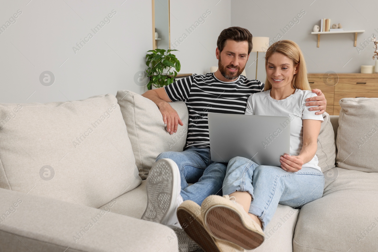 Photo of Happy couple with laptop on sofa at home. Space for text