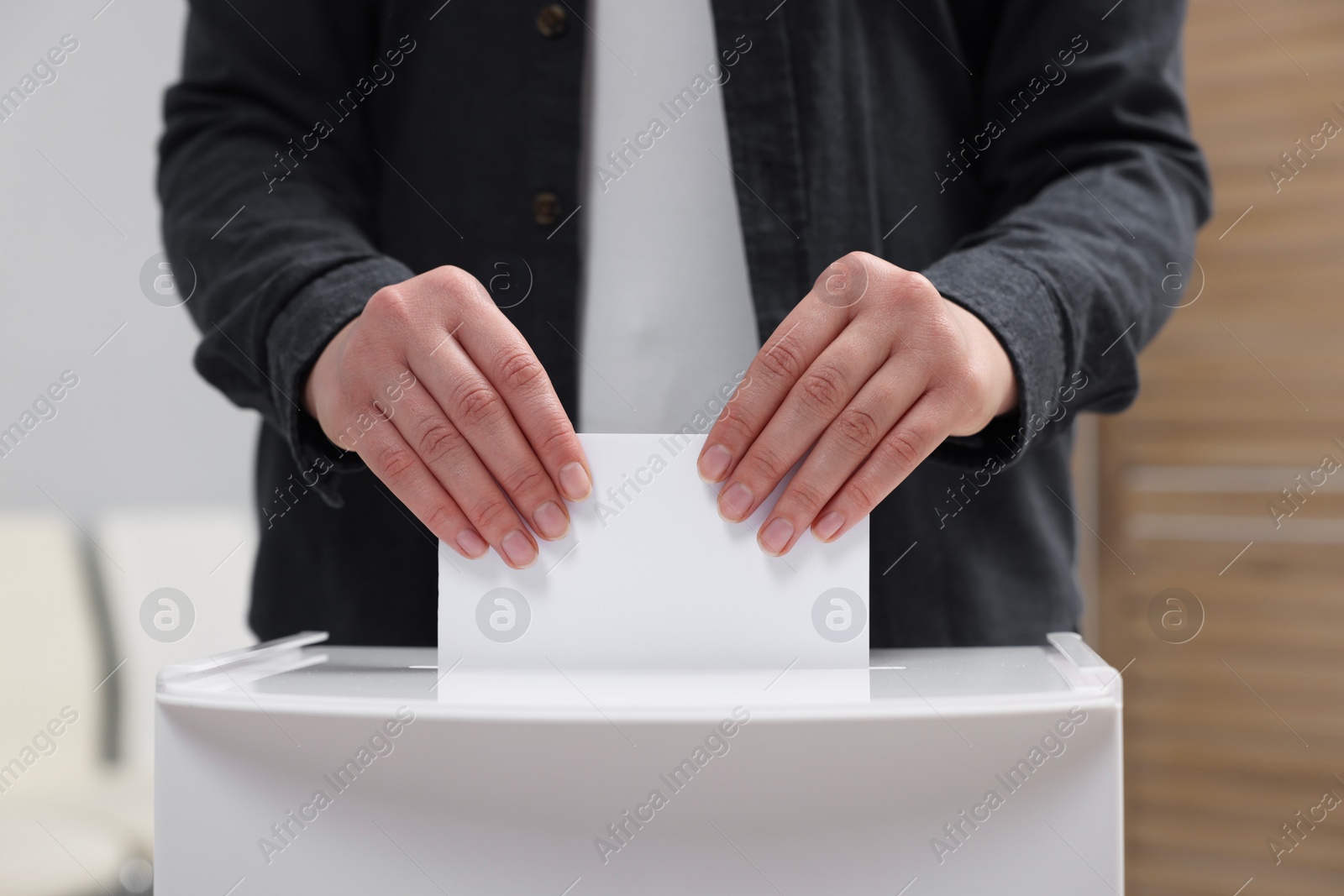 Photo of Woman putting her vote into ballot box on blurred background, closeup