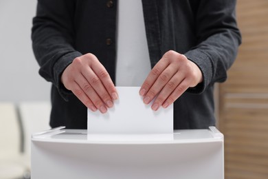 Photo of Woman putting her vote into ballot box on blurred background, closeup