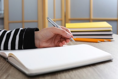 Photo of Woman writing in notebook at wooden table indoors, closeup