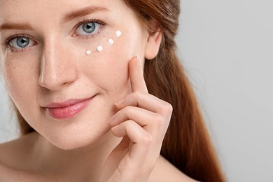 Beautiful woman with freckles and cream on her face against grey background, closeup. Space for text