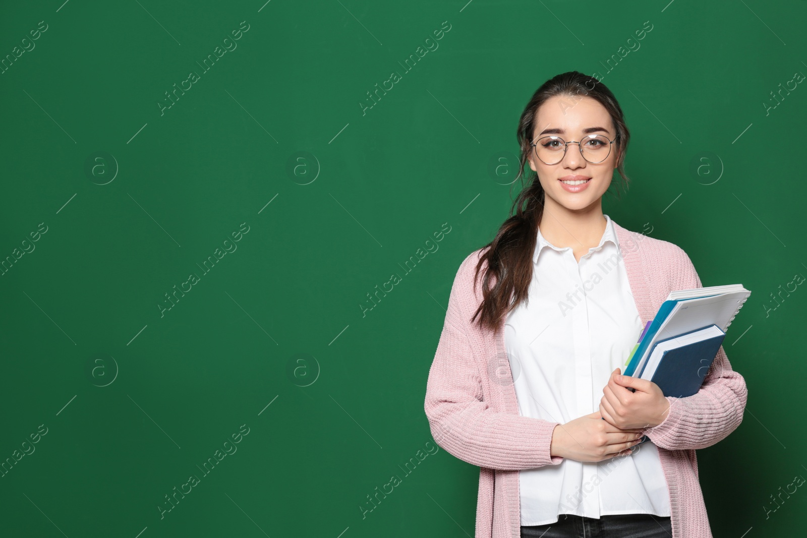 Photo of Portrait of beautiful young teacher with books near chalkboard, space for text