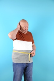 Fat senior man with measuring tape on color background. Weight loss