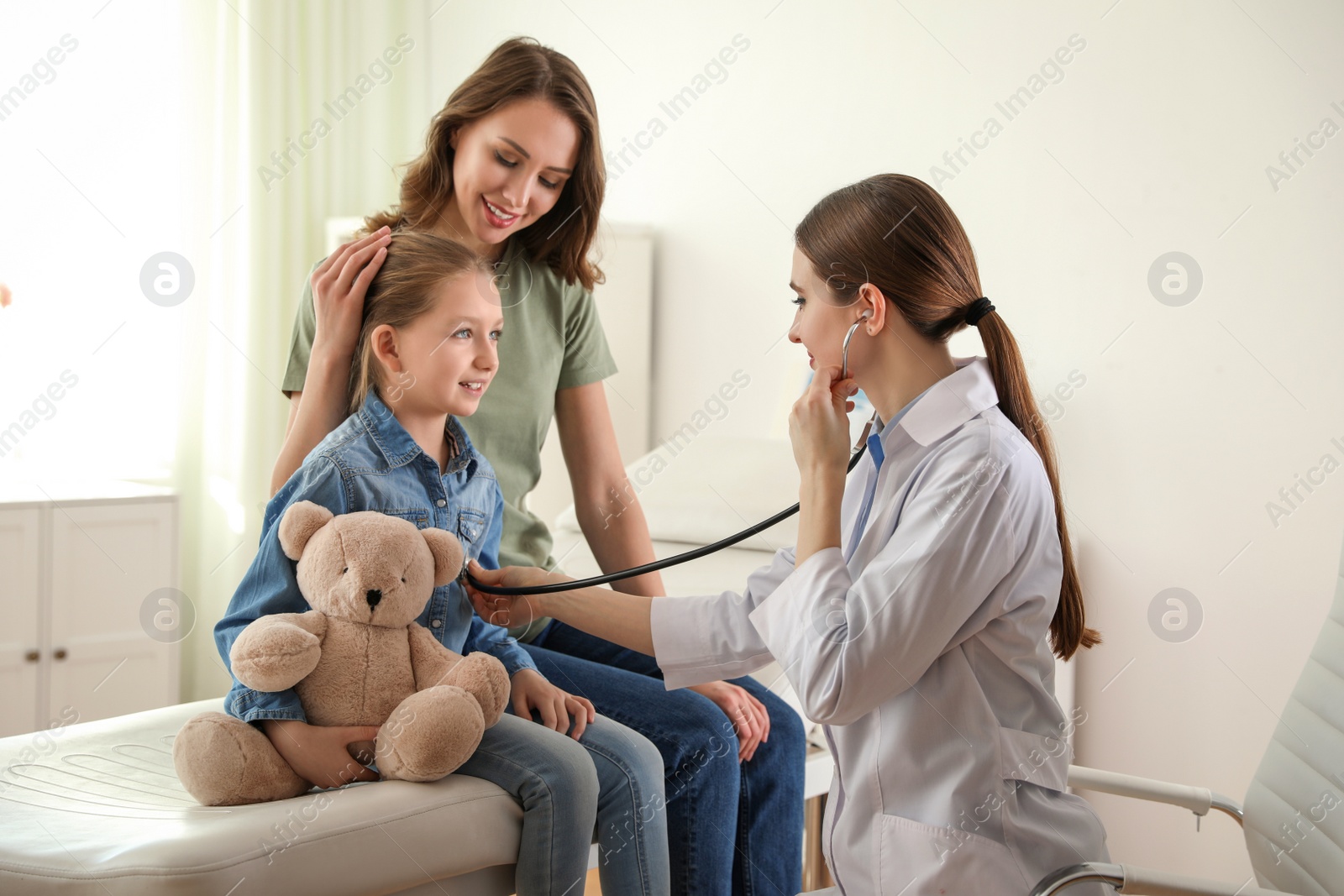 Photo of Mother and daughter visiting pediatrician. Doctor examining little patient with stethoscope in hospital