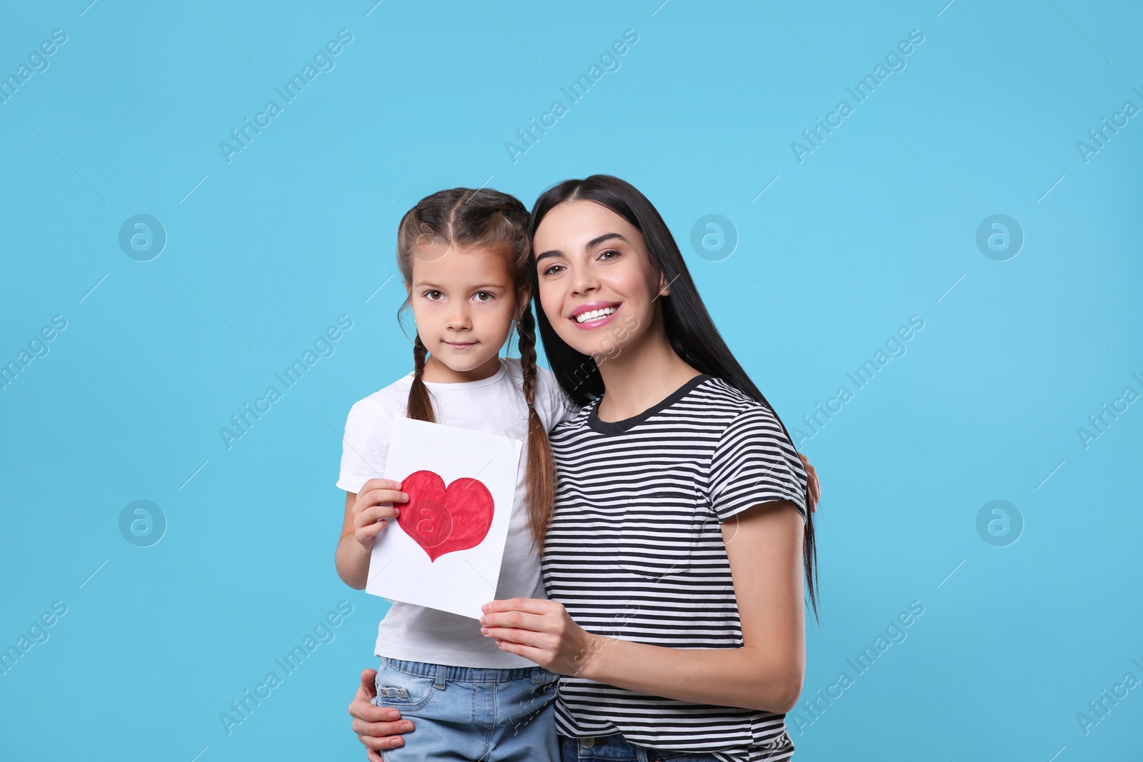Photo of Happy woman with her cute daughter and handmade greeting card on light blue background. Mother's day celebration