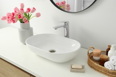 Photo of Vase with beautiful pink tulips and toiletries near sink in bathroom