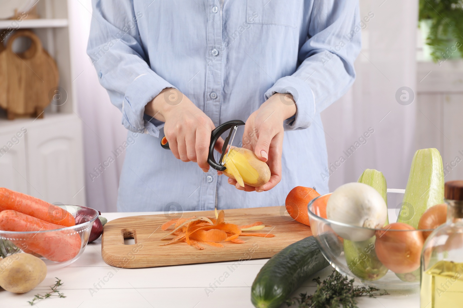 Photo of Woman peeling fresh potato at white wooden table indoors, closeup