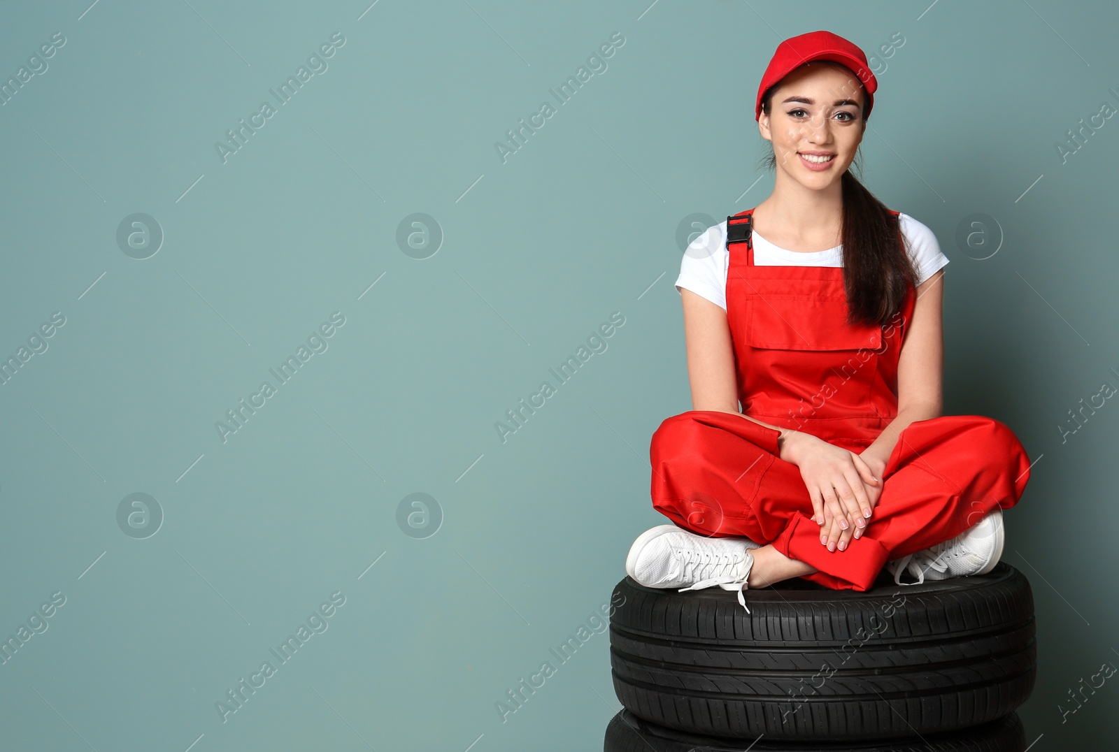 Photo of Female mechanic in uniform with car tires on color wall background