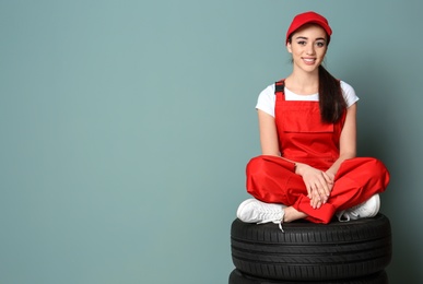 Female mechanic in uniform with car tires on color wall background