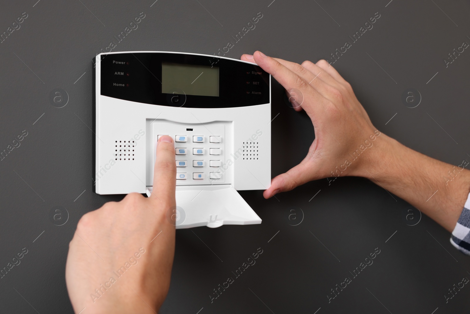 Photo of Man entering code on home security alarm system near gray wall, closeup