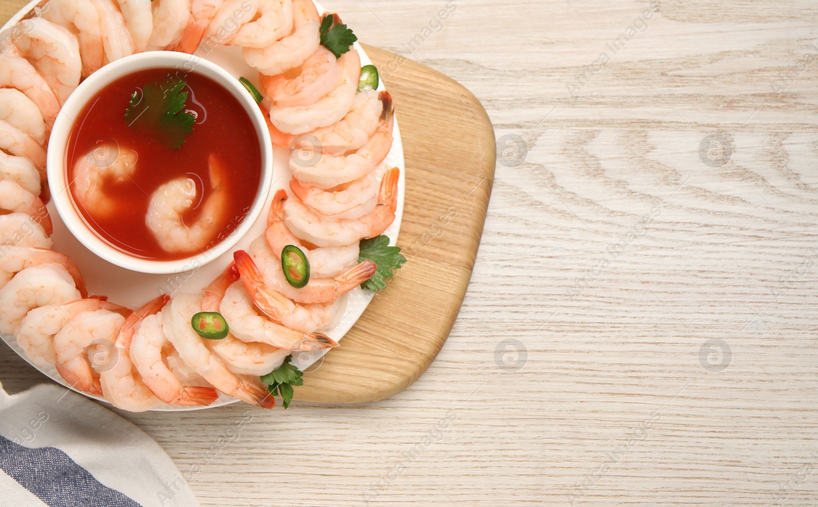 Photo of Tasty boiled shrimps with cocktail sauce, chili and parsley on light wooden table, top view. Space for text