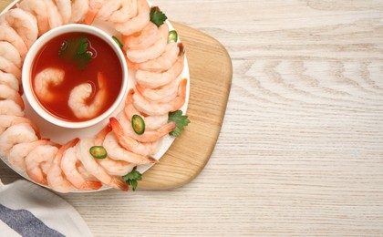 Photo of Tasty boiled shrimps with cocktail sauce, chili and parsley on light wooden table, top view. Space for text