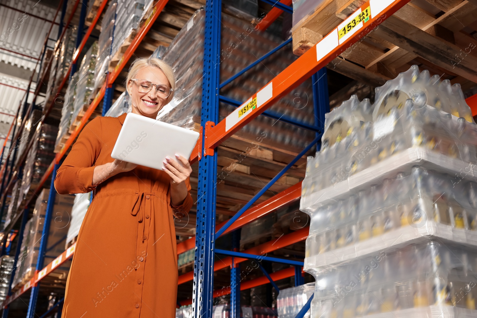 Photo of Happy manager using modern tablet in warehouse with lots of products, low angle view