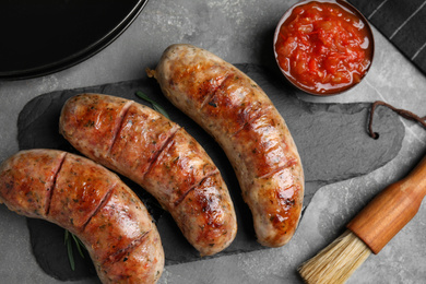 Tasty grilled sausages served on grey table, flat lay