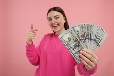 Photo of Happy woman pointing at dollar banknotes on pink background, selective focus