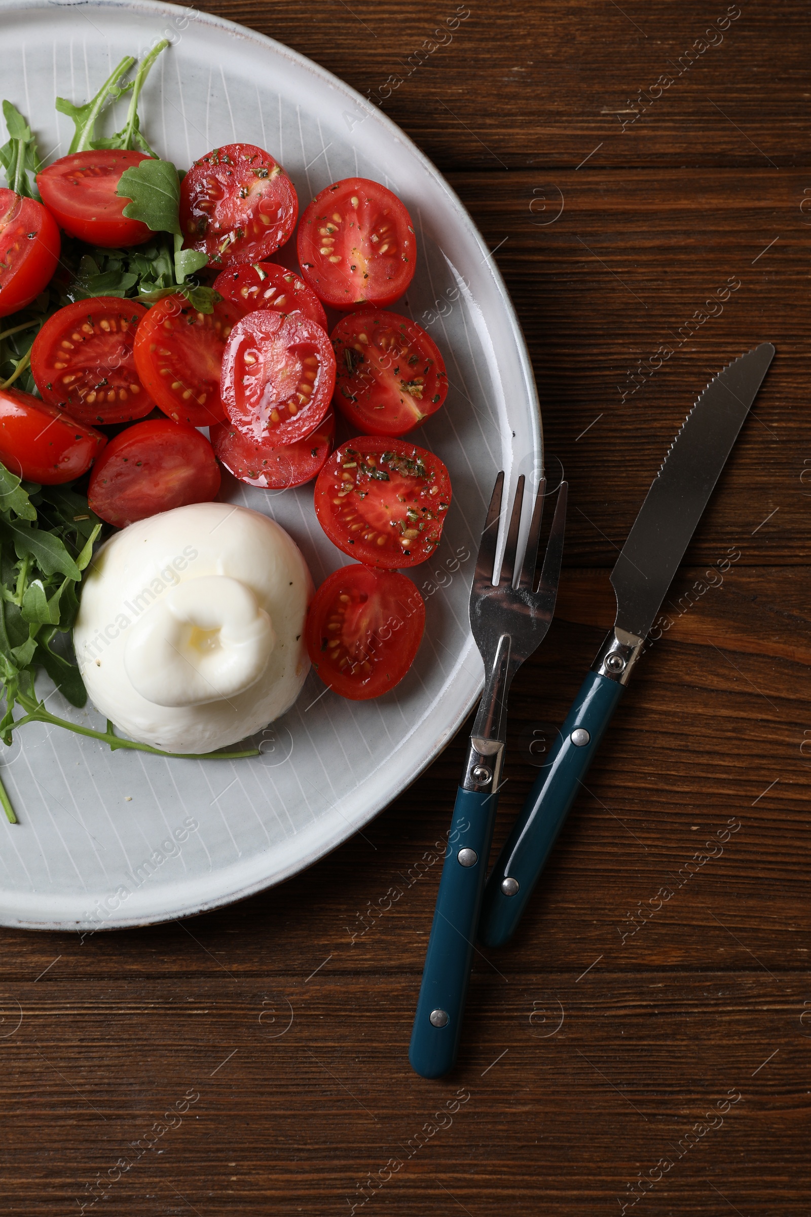 Photo of Delicious burrata cheese with tomatoes and arugula served on wooden table, top view