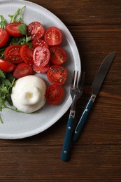 Delicious burrata cheese with tomatoes and arugula served on wooden table, top view