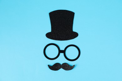 Photo of Man's face made of fake mustache, hat and glasses on light blue background, top view
