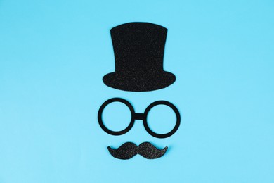 Man's face made of fake mustache, hat and glasses on light blue background, top view