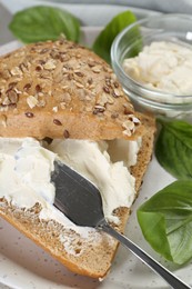 Pieces of bread with cream cheese and basil leaves on plate, closeup