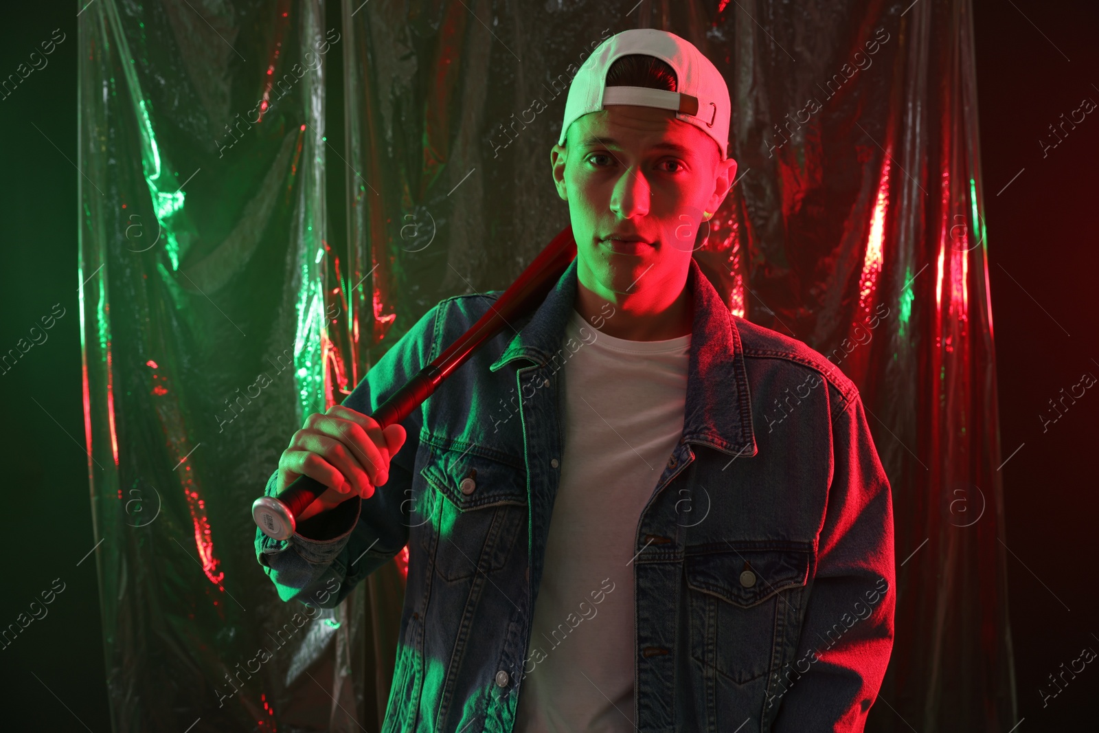 Photo of Young man with baseball bat on dark background in neon lights