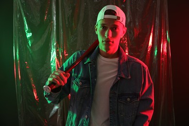 Photo of Young man with baseball bat on dark background in neon lights