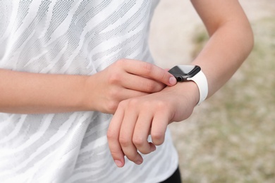 Photo of Young woman checking pulse with smartwatch after training outdoors, closeup