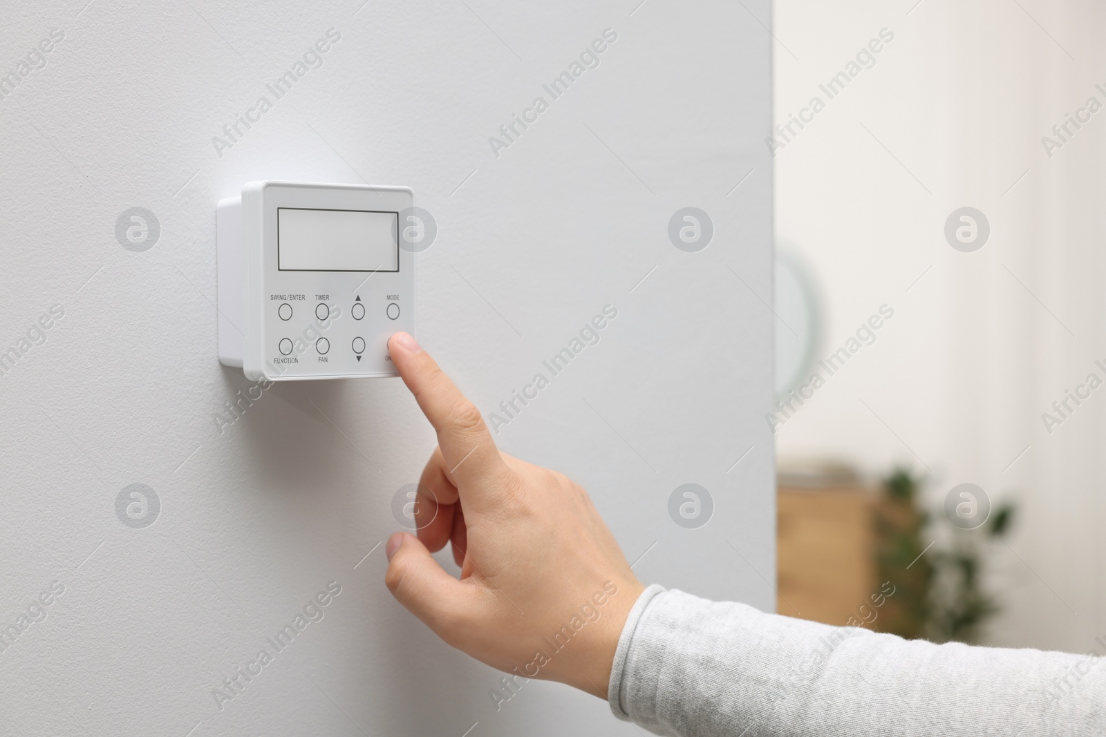 Photo of Woman adjusting thermostat on white wall indoors, closeup. Smart home system