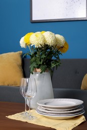 Vase with beautiful flowers, glasses and plates on wooden table in living room. Interior element