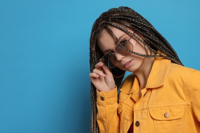 Photo of Beautiful woman with long african braids and sunglasses on blue background, space for text
