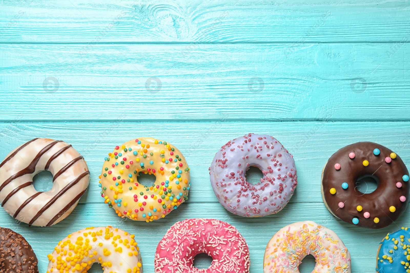 Photo of Delicious glazed donuts on blue wooden table, flat lay. Space for text