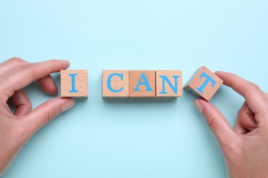 Photo of Motivation concept. Woman changing phrase from I Can't into I Can by removing wooden cube with letter T on light blue background, top view