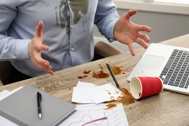Photo of Man with spilled coffee over his workplace and shirt, closeup