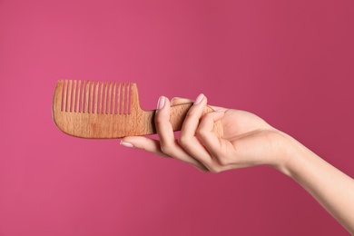 Photo of Woman holding wooden hair comb against crimson background, closeup