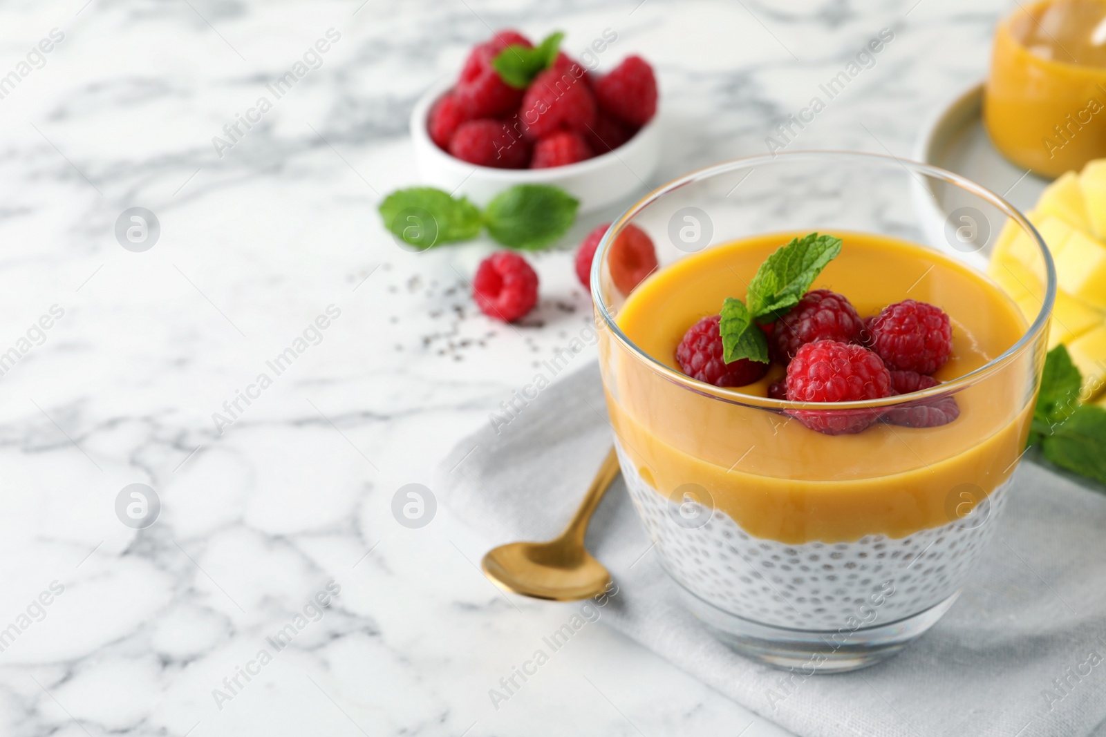 Photo of Delicious chia pudding with mango sauce and raspberries on white marble table. Space for text