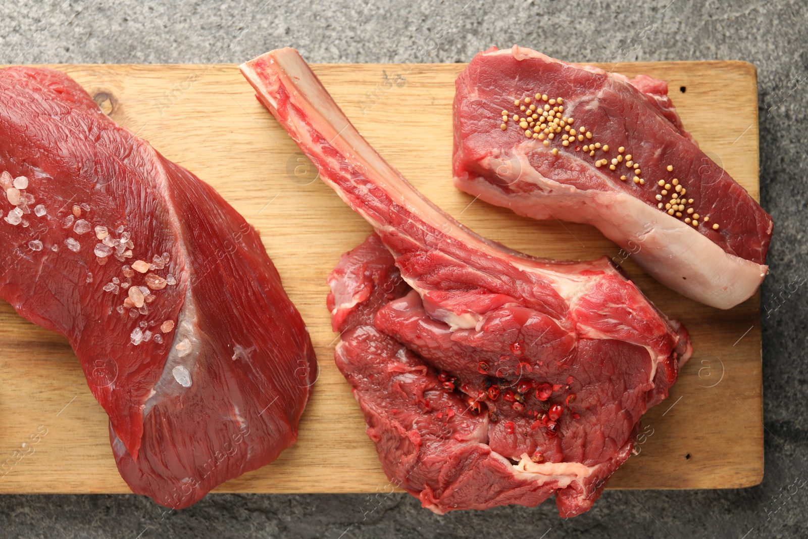 Photo of Pieces of raw beef meat and spices on grey textured table, top view