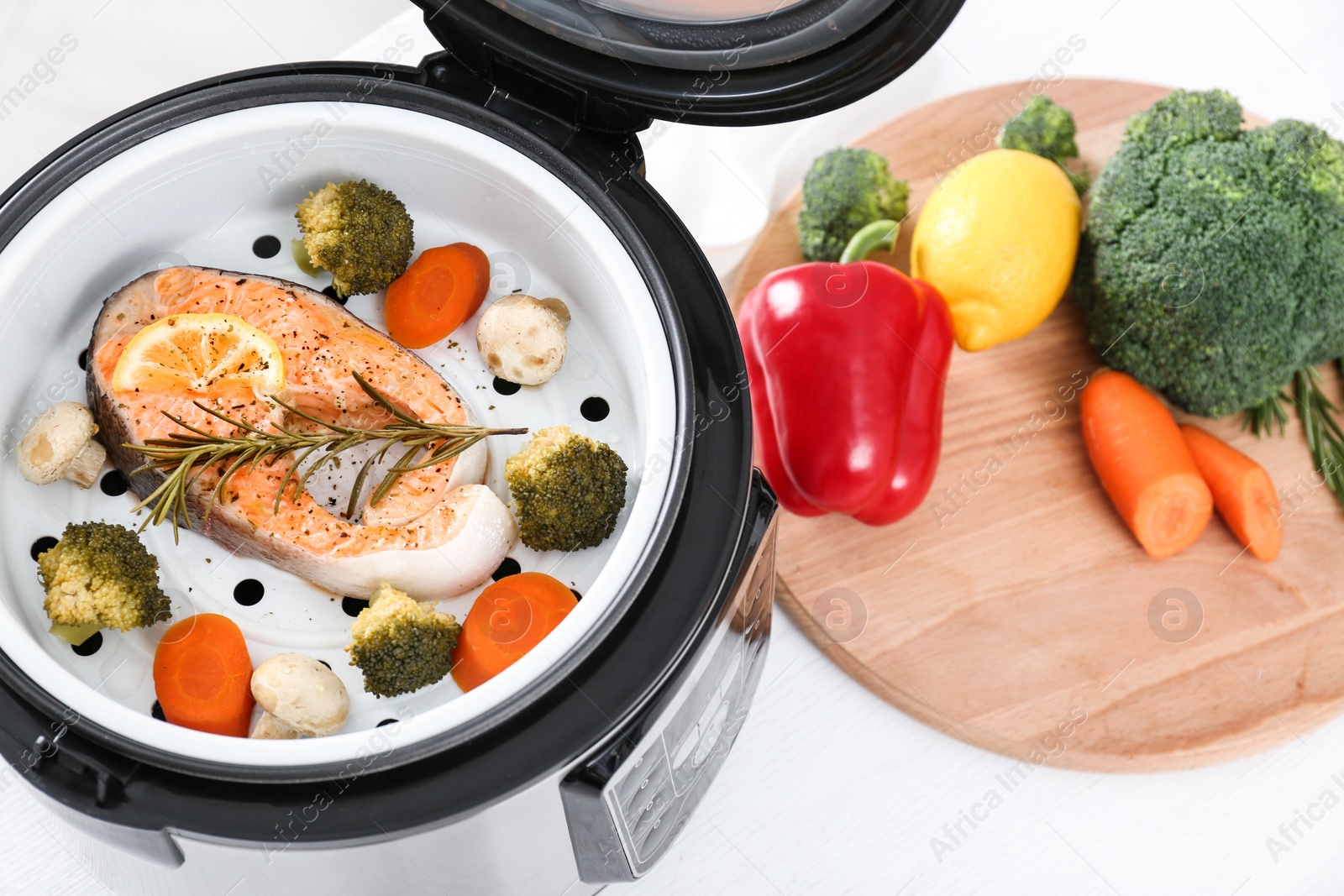 Photo of Multi cooker with salmon steak and garnish on white table, above view