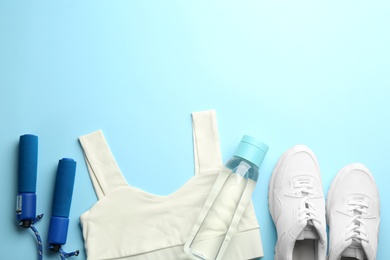 Photo of Sportswear, jump rope and water bottle on light blue background, flat lay with space for text. Gym workout