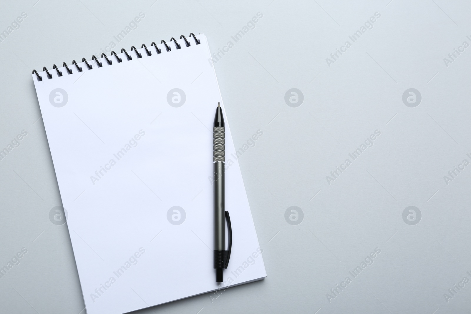 Photo of One notebook and pen on light grey background, top view. Space for text