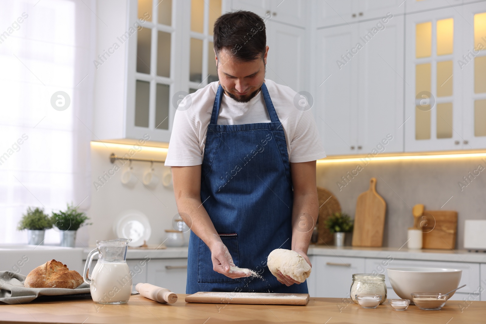 Photo of Making bread. Man sprinkling flour onto dough at wooden table in kitchen