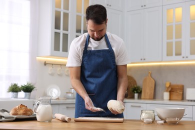 Photo of Making bread. Man sprinkling flour onto dough at wooden table in kitchen