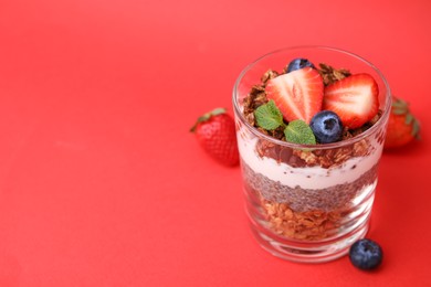 Photo of Tasty granola with berries, yogurt and chia seeds in glass on red background, closeup. Space for text