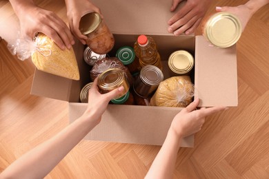 Group of volunteers packing food products at wooden table, top view