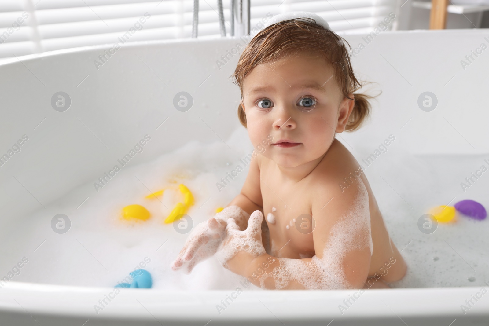 Photo of Cute little girl taking bubble bath with toys indoors