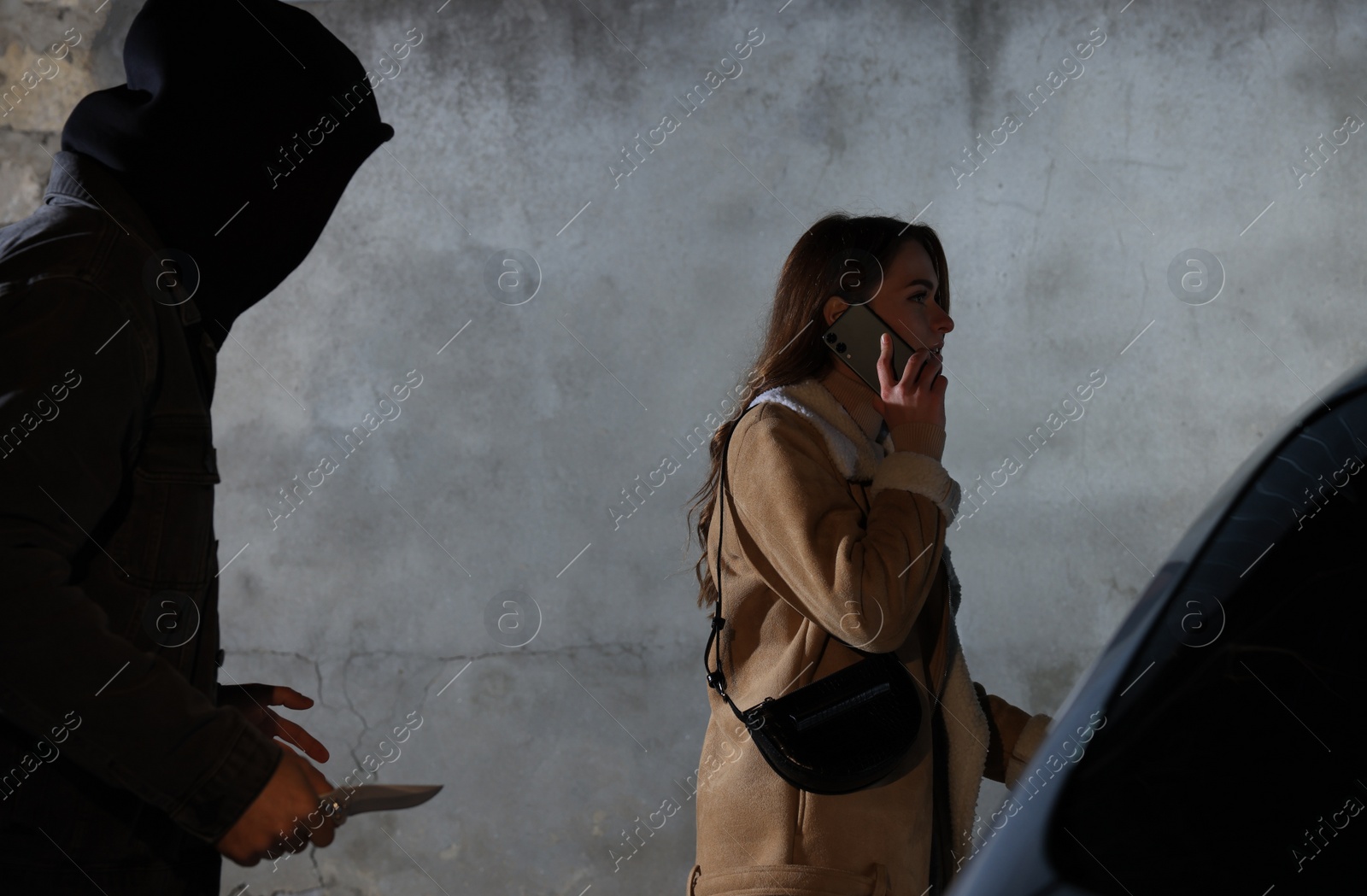 Photo of Man with knife stalking young woman while she talking on phone near car