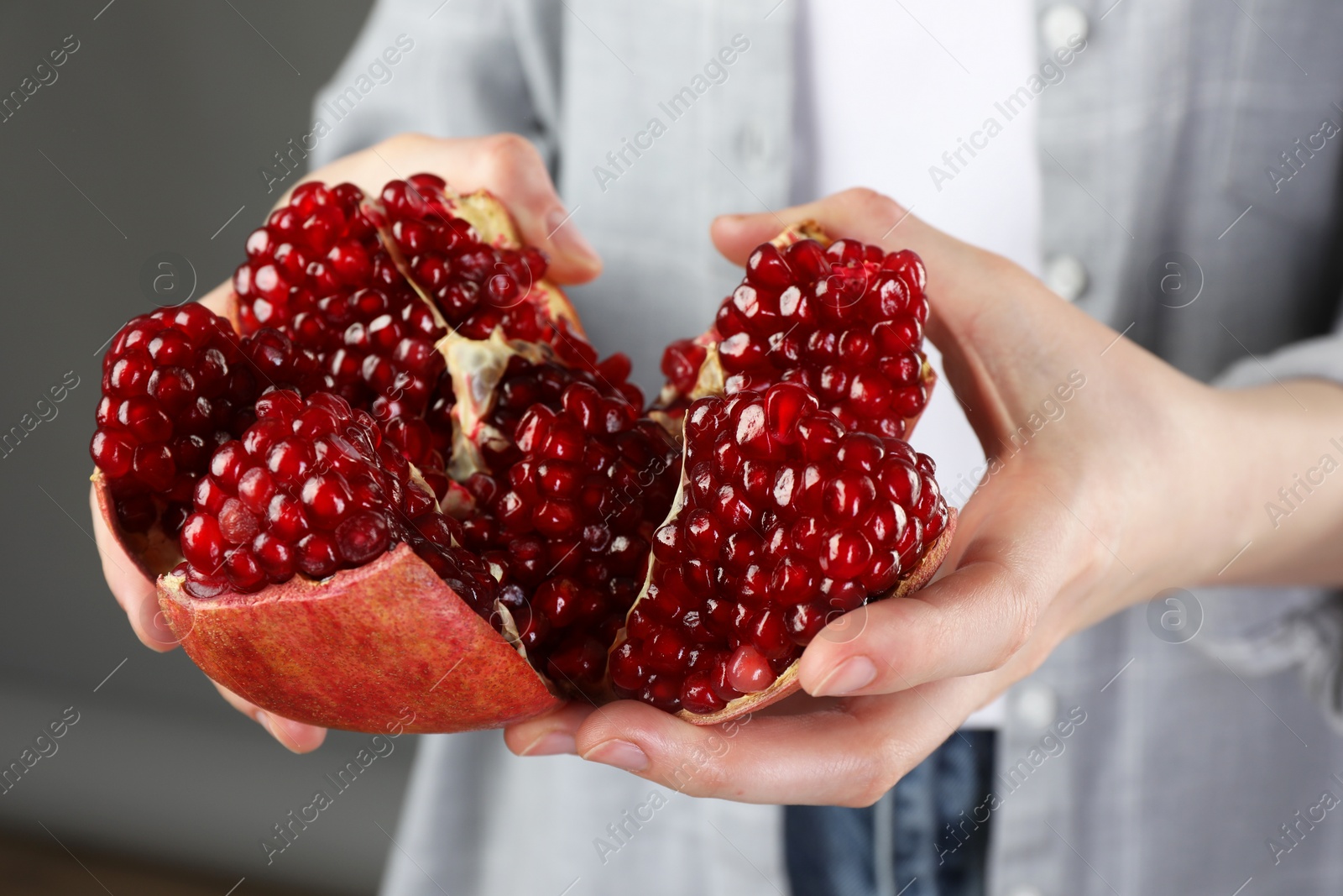 Photo of Woman holding fresh pomegranate on grey background, closeup