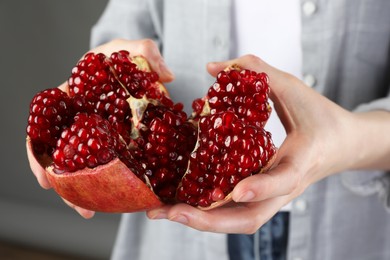 Photo of Woman holding fresh pomegranate on grey background, closeup