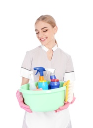 Young chambermaid holding plastic basin with detergents on white background